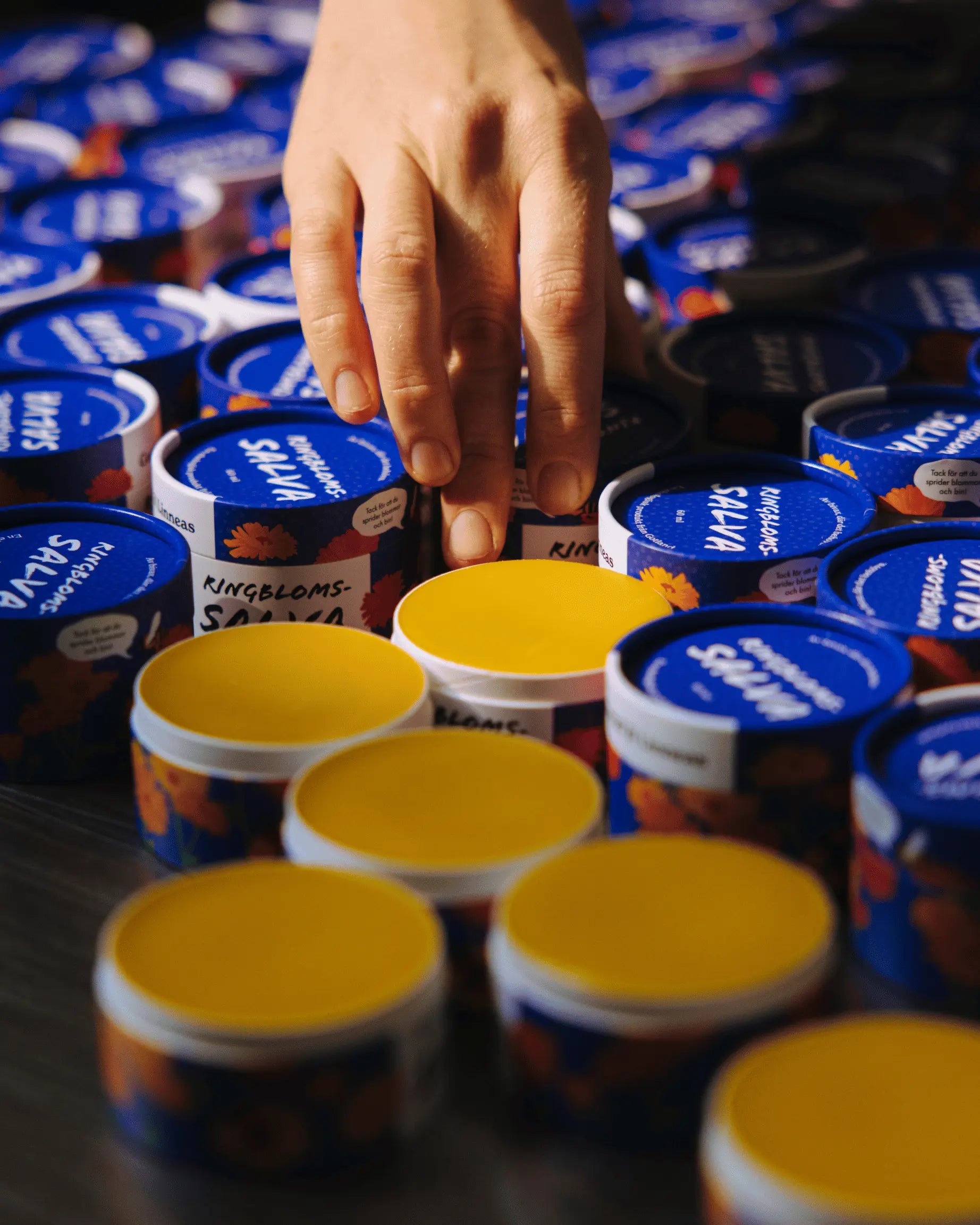 En hand som lägger lock på nytillverkade ringblomssalvor.