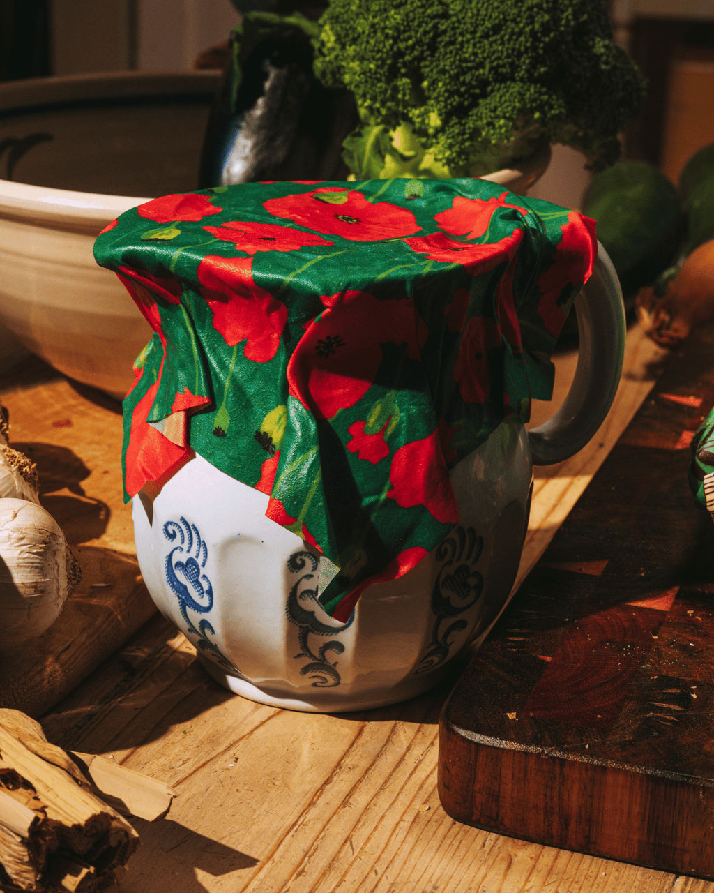 En bivaxduk med motiv av vallmo trädd över en kanna i ett kök.